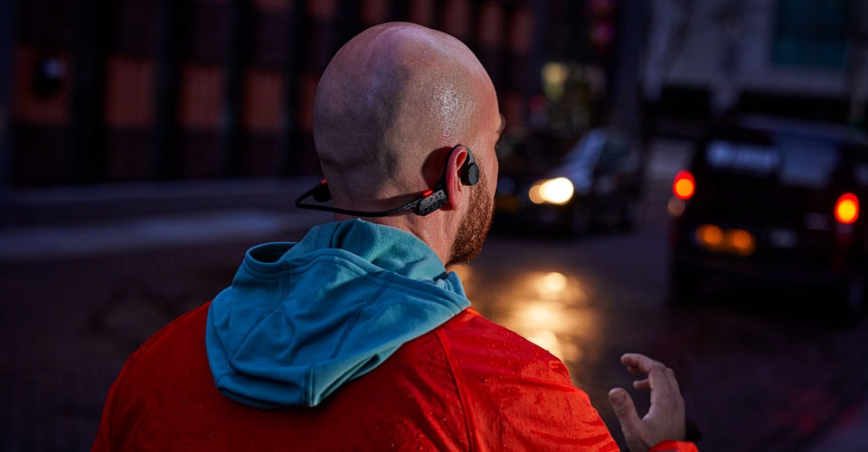 muž nosí sluchátka s otevřeným uchem na přeplněné ulici