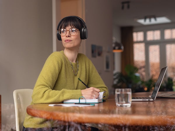 Osoba v pohodlných Philips sluchátkách sedí u stolu s notebookem a laptopem