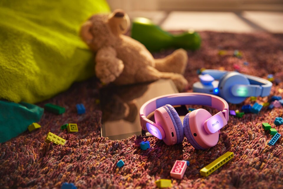 Dvoje dětská sluchátka, modrá a růžová, na zemi vedle hraček.