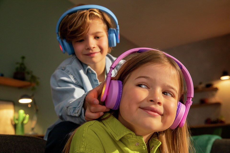 Dva sourozenci hrající si při používání dětských sluchátek na uši.