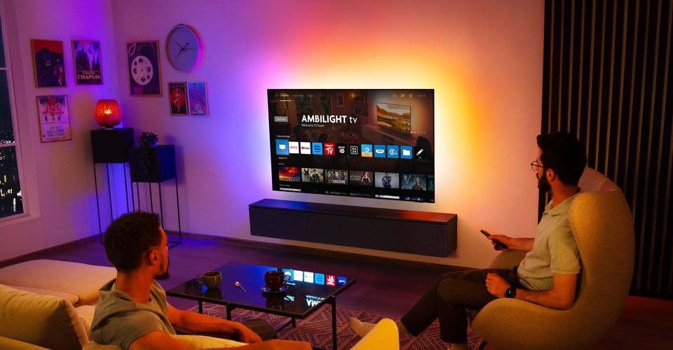 Dva muži sledují nástěnný televizor Ambilight v obývacím pokoji