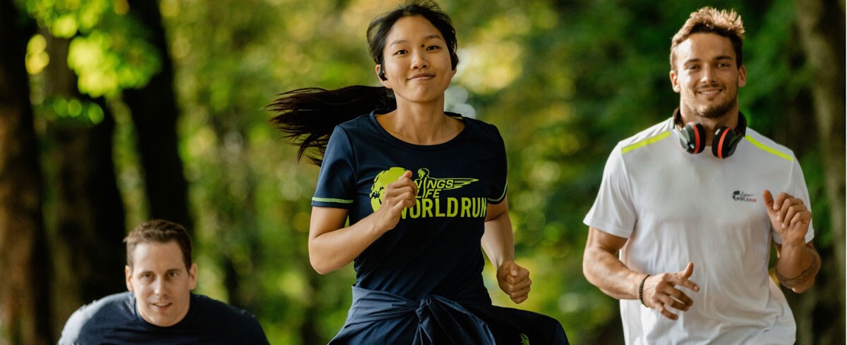 Tři běžci běhu Wings for Life World Run, kteří vesele běží s nasazenými sportovními sluchátky Philips.