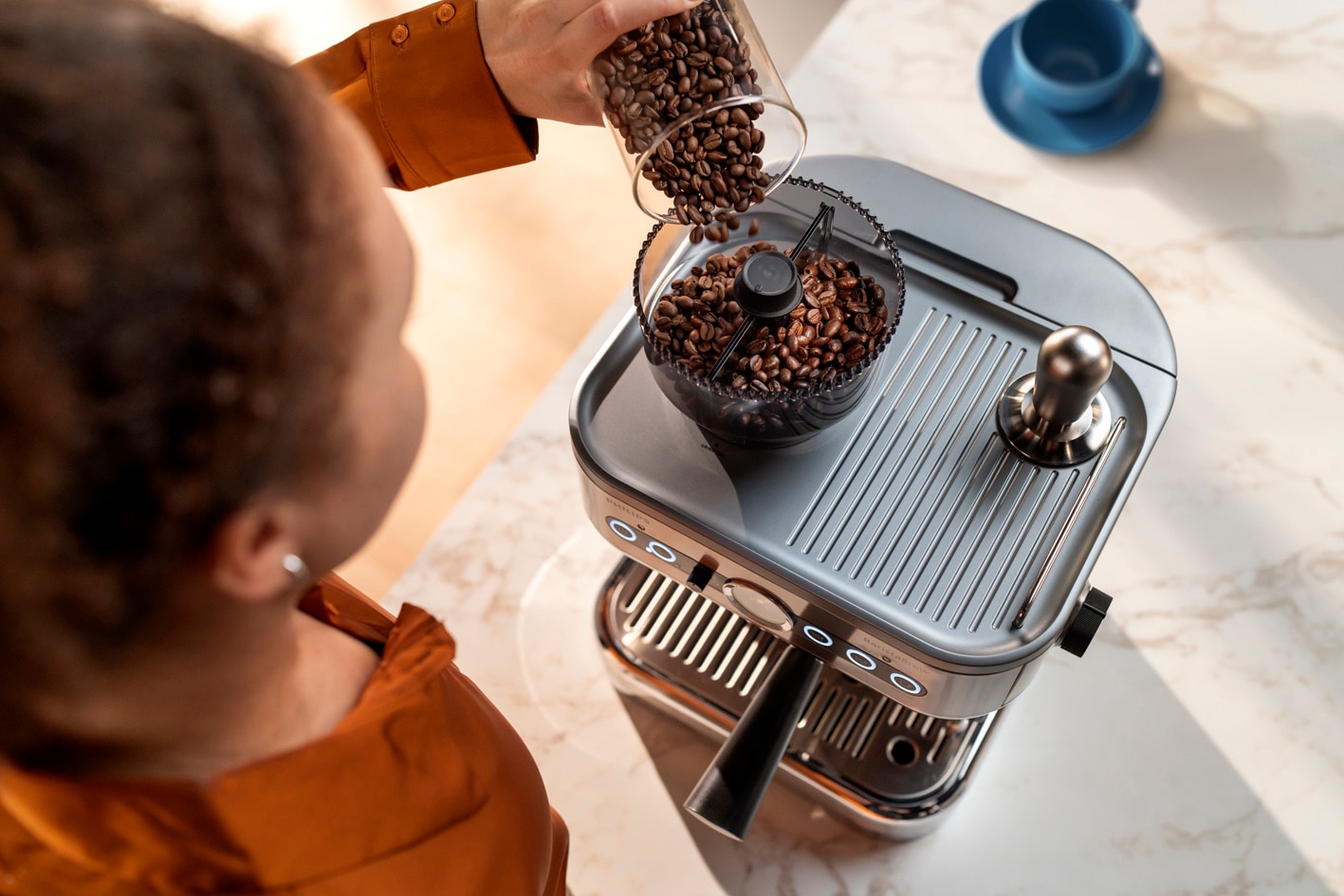 Mladá žena sype zrnkovou kávu do nádoby na kávová zrna kávovaru Philips Barista Brew