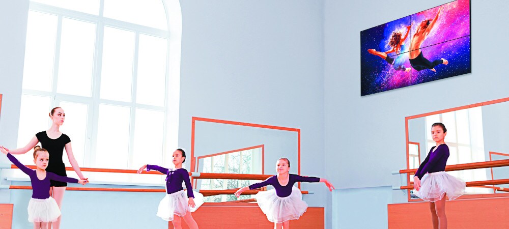 Displej s digitální prezentací na stěně. Děti se učí tančit balet v místnosti